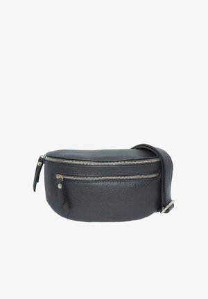 Femme portant un haut noir à manches longues, un jean noir et un sac à bandoulière en cuir noir avec deux fermetures éclair argentées sur la poitrine.