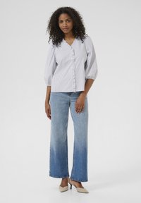 Camicia a righe con bottoni, scollatura a V e maniche a sbuffo, abbinata a jeans in denim a gamba larga con sfumatura ombré e décolleté beige a punta.