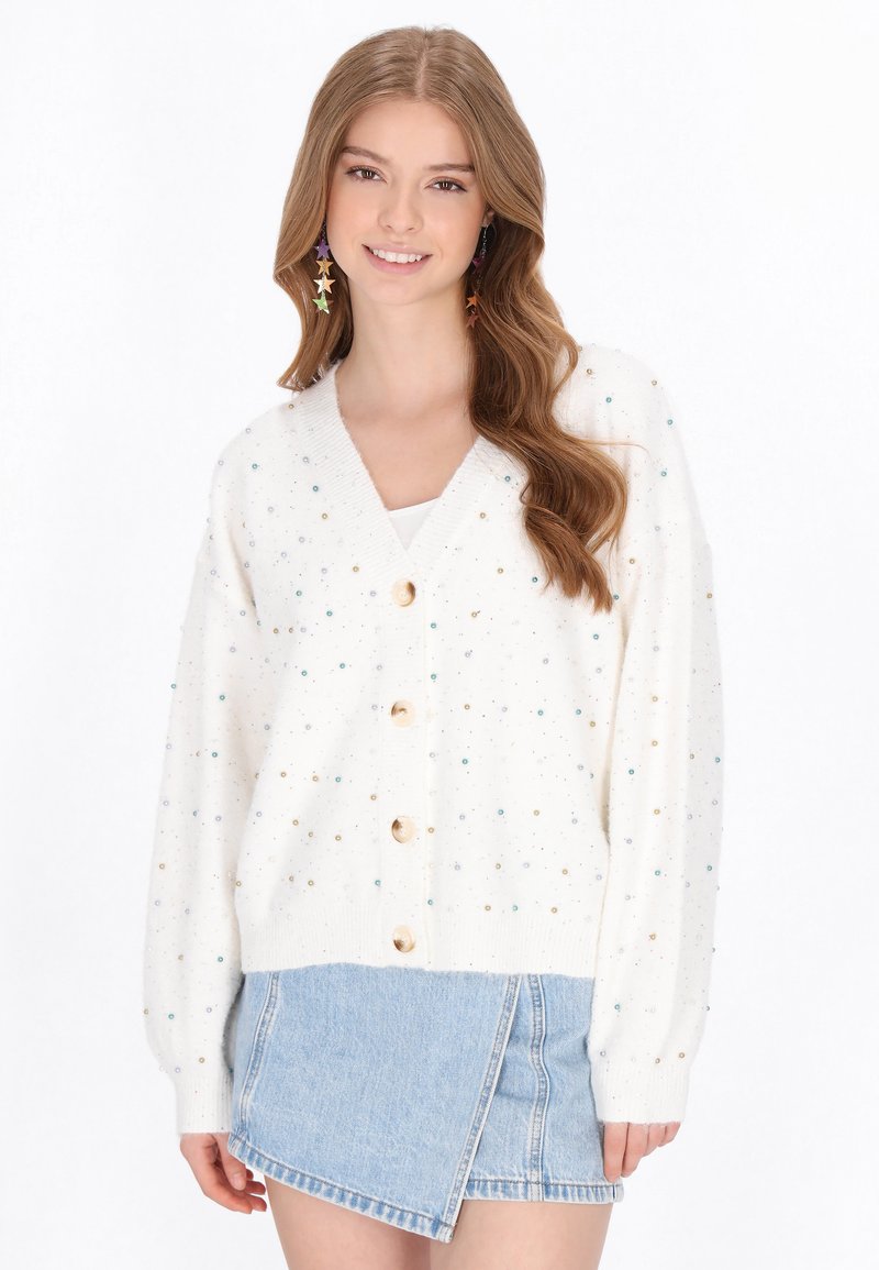 Tej színű kardigán színes pettyekkel, hosszú ujjak, V-nyakú és öt fából készült gombbal. Világoskék farmer szoknyával párosítva.