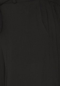 Svart tyg med en jämn textur. Har en midjeband och veck på ena sidan, vilket visar en enkel, minimalistisk design.