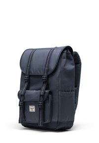 Ruksak od tamnoplave tkanine s preklopnim zatvaračem, dva prednja remena, bočnim džepovima i teksturiranom stražnjom stranicom za udobnost. Logotip na prednjem dijelu.