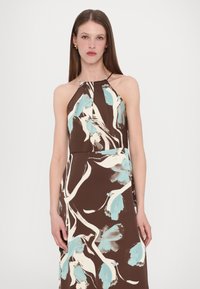 Robe sans manches marron avec des motifs floraux bleus et blancs, dotée d'un col halter et d'une silhouette élancée. Texture de tissu lisse.