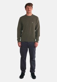 Suéter de punto verde oliva con puños y dobladillo acanalados, combinado con pantalones oscuros y zapatos negros. Corte casual, tejido texturizado, detalle de marca mínimo.