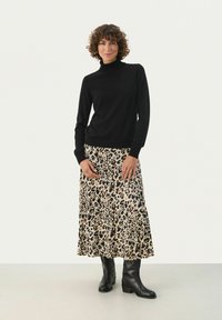 Črn pulover s turtleneck ovratnikom v kombinaciji z rahlo krilno kremno krilo, ki ima vzorec leoparda. Manekenka nosi črne škornje do kolen.