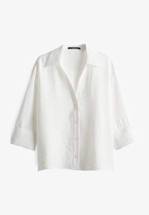Chemise blanche à manches trois-quarts, avec un col pointu et un tissu texturé. Comprend cinq boutons et une coupe décontractée.
