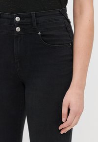 Melnas augstās jostas bikses ar elegantu dizainu, kas aprīkotas ar diviem sudraba pogām un priekšējo kabatu. Audumam ir gluda tekstūra.