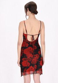 Vestido negro con estampados florales rojos, textura transparente, tirantes finos y una espalda baja con cierre de lazo. Detalle de dobladillo con forma de onda.