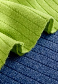 Zaļš ribots audums ir uzklāts uz teksturēta zila auduma, abi izceļot mīkstu adījumu ar izteiktām vertikālām svītrām.