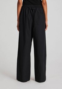 Black wide-leg pants with an elastic waistband, featuring a back pocket, made from a lightweight fabric with a smooth texture.