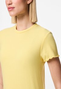 Dzeltena riboto t-kreklu ar īsām, zvana formas piedurknēm un apaļu izgriezumu. Audums ir mīksts un pieguļošs.