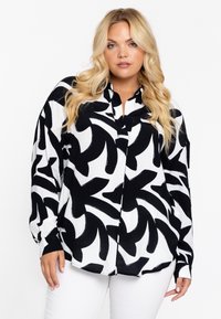 Schwarz-weiße Bluse mit einem auffälligen abstrakten Muster, langen Ärmeln, einem kragenförmigen Ausschnitt und einer lockeren Passform. Glattes Material mit leichtem Glanz.