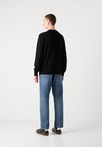 Zwarte lange mouwen trui met ribgebreide manchetten en zoom, gedragen met lichtblauwe rechte jeans en zwarte sneakers, gezien van achteren.