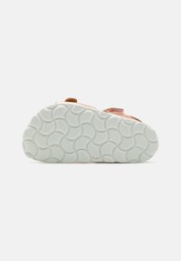 Lichtroze sandaal met een gestructureerde beige band en een gestructureerde witte rubberen zool met een golfpatroon. Verstelbare sluiting voor een goede pasvorm.