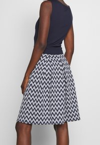 Granatowy top bez rękawów w połączeniu z spódnicą do kolan, ozdobioną wzorem w zygzak w granacie i bieli. Spódnica ma fałdowany krój i gładką fakturę.