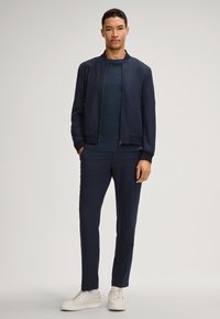 Marine bomberjack met een rits, bijpassend marine T-shirt en tailored broek, gecombineerd met witte sneakers. Soepele stof, minimalistisch ontwerp.