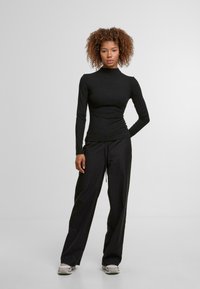 Čierny dlhý rukáv s rolákom v páre s voľnými čiernymi nohavicami, oboje z hladkej látky, nosené so sivými športovými topánkami.