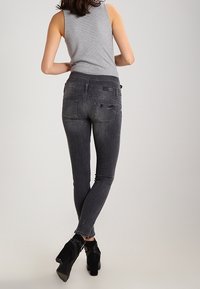 Úzké tmavě šedé džíny s hladkým texturem, vybavené zadními kapsami a jemným blednutím. Kombinované s černými kotníkovými botami pro zdůraznění.
