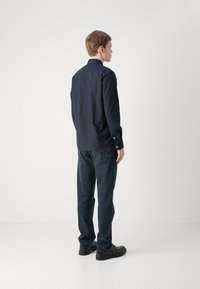 Marineblauw overhemd met kraag, gecombineerd met donkerblauwe jeans. De stof lijkt glad, en de schoenen zijn zwart met een ronde neuzenontwerp.