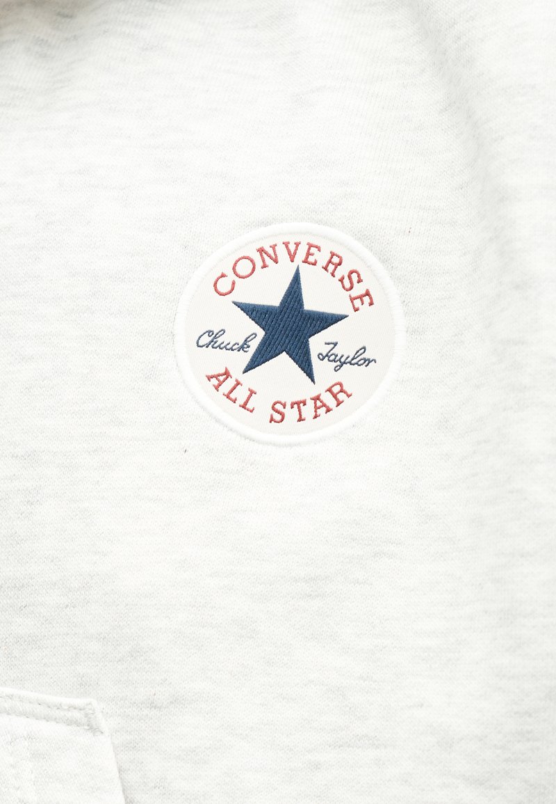 Witte stof met een genaaide, ronde Converse All Star-patch met een blauwe ster en rood- en blauwkleurige tekst.