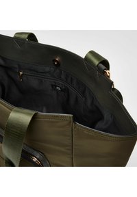 Grøn nylontotebag med sort indre, der har en lynlås lomme, syede detaljer og dobbelte top-håndtag. Lukkemekanismen er en trykknap.