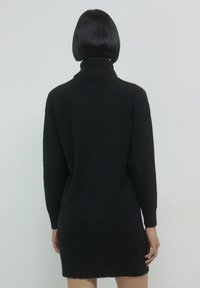 Schwarzes Strickkleid mit hohem Kragen, langen Ärmeln, gerippten Bündchen und Saum, aus einem weichen, strukturierten Stoff mit figurbetontem Schnitt.