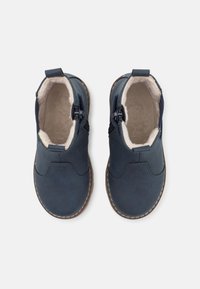 Ett par marinblå barnankelboots med sidodragkedja och creamfärgad fleecefoder, sedd ovanifrån på vit bakgrund.