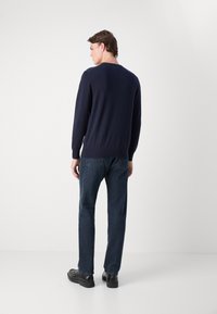 Dunkelblauer, gestrickter Pullover mit V-Ausschnitt, langen Ärmeln und gerippten Bündchen. Kombiniert mit dunklen Jeans und schwarzen Schuhen.
