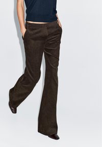 Bruine corduroy broek met een uitlopende stijl, voorzien van zijzakken en een gestructureerd oppervlak, gecombineerd met donkere hakken.