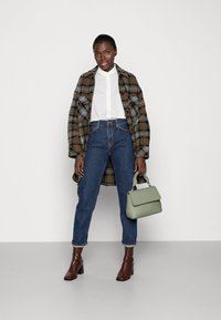 Cappotto di lana a quadri marrone e grigio, camicia bianca, jeans in denim blu, stivali con tacco marroni e borsa verde chiaro.