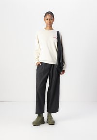Sudadera crema con texto rojo, pantalones de pierna ancha grises y botas de plataforma verde oliva. Modelo sosteniendo un bolso negro de hombro.