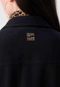 Schwarze Jacke mit einem Kragen aus Leopardenmuster. Verfügt über einen strukturierten Stoff, sichtbare Nähte und ein kleines Markenemblem in einer kontrastierenden Farbe.