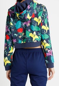Felpa cropped con uno sfondo blu navy caratterizzata da festoni floreali colorati in giallo, rosso e verde. Abbinata a pantaloni elasticizzati blu navy.