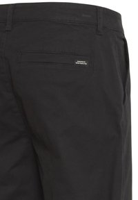 Black pants featuring a rear pocket with a small, rectangular label that reads "DEDICATED TO DENIM PERFECTION." The fabric has a smooth texture.