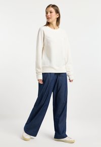 Felpa dalla texture cremosa con maniche lunghe, abbinata a pantaloni in denim scuri a vestibilità ampia e sneaker bianche.