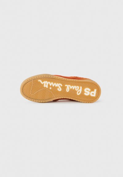 Sole di una scarpa in suede arancione con motivo di battistrada in gomma e branding bianco "PS Paul Smith" sul fondo.