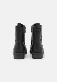 Mustad mustad nahast ankle saapad tekstuuriga pinnaga, külgmiste lukudega ja platvormi kontsaga. Omab diskreetset õmblust ning tõmblukke mugavaks selga panemiseks.