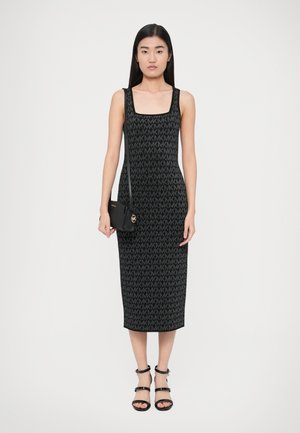 Sort strikket kjole med firkantet udskæring, prydet med et gennemgående logo mønster, kombinert med en lille sort crossbody-taske og sorte sandaletter med stropper.