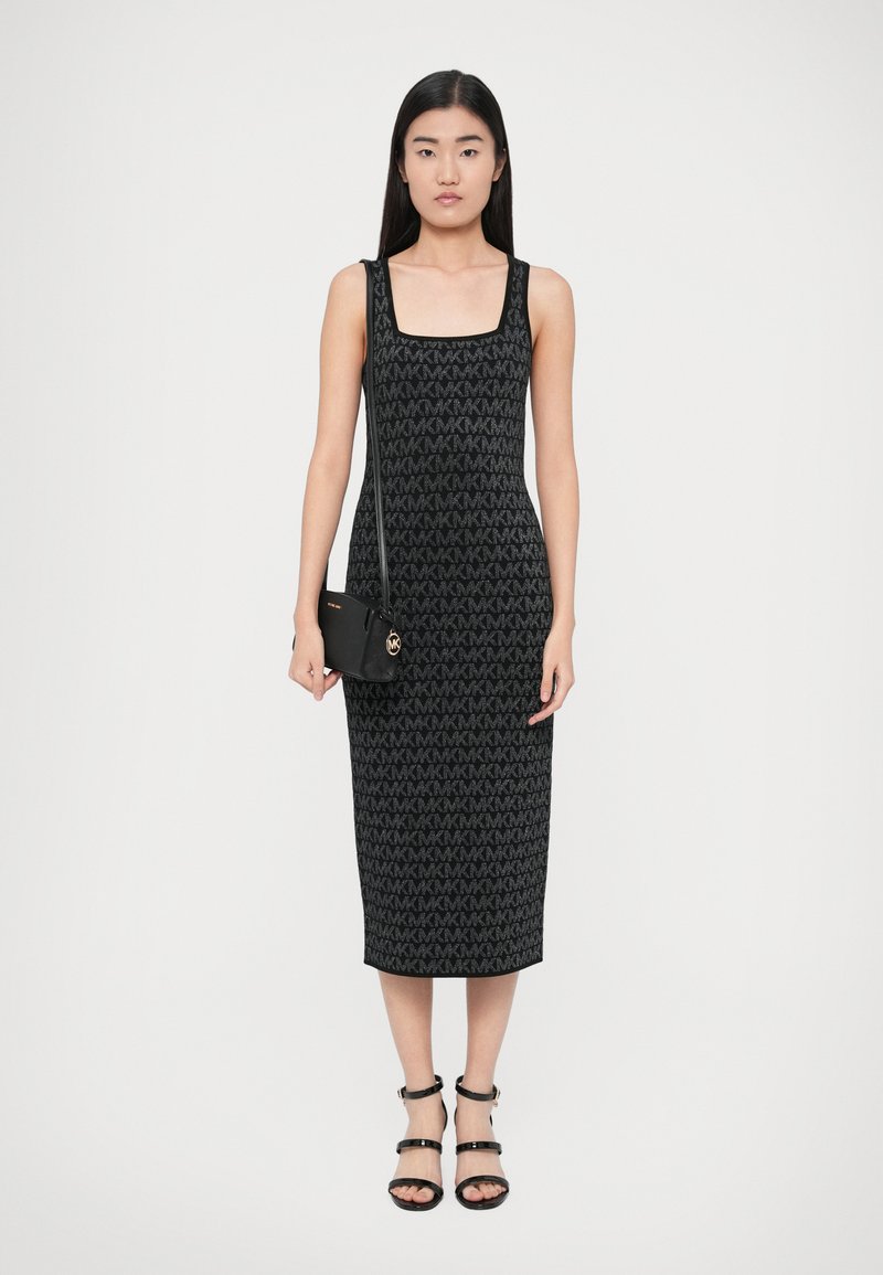 Schwarzes Strickkleid mit quadratischem Ausschnitt, das ein durchgängiges Logo-Muster zeigt, kombiniert mit einer kleinen schwarzen Umhängetasche und schwarzen Riemchensandalen.