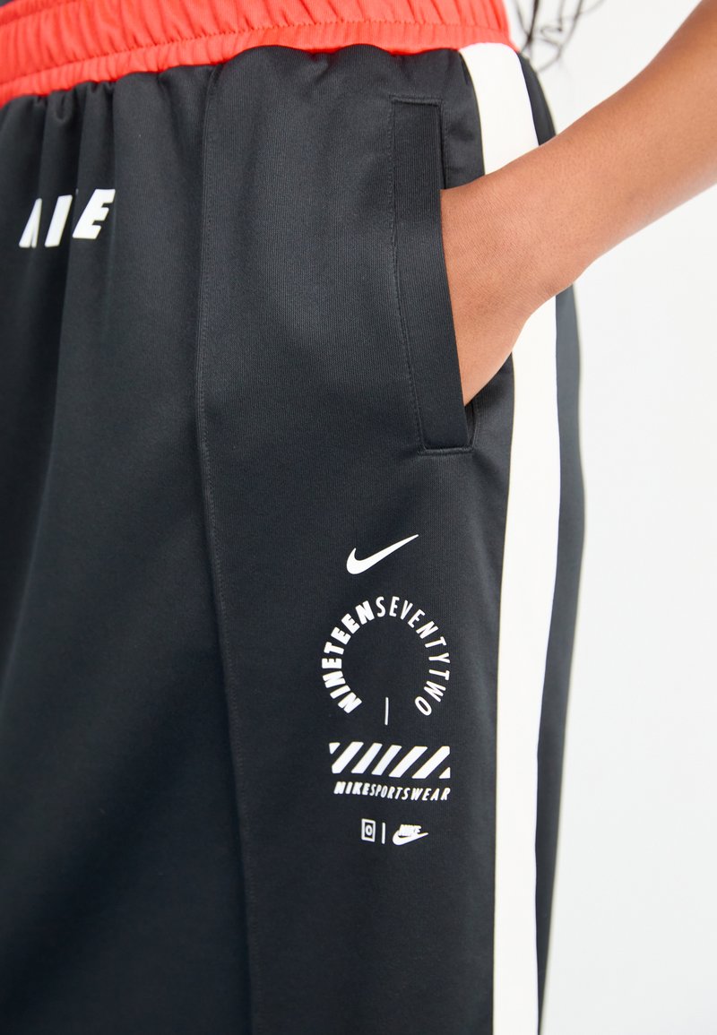 Pantalones deportivos negros con cintura elástica roja, que cuentan con un logo blanco y un estampado gráfico en la pierna izquierda y bolsillos laterales.