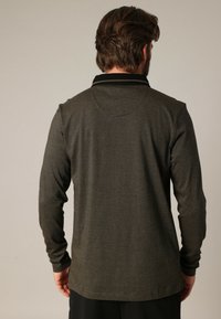 Langärmliges Poloshirt in Dunkelgrün mit einem strukturierten Streifenmuster, ausgestattet mit einem schwarzen Kragen und einem lockeren Schnitt.