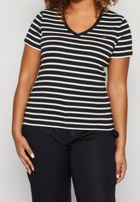 T-shirt a maniche corte con scollo a V a righe blu navy e crema, con bordo a fascia solido, caratterizzata da un piccolo logo sul petto.