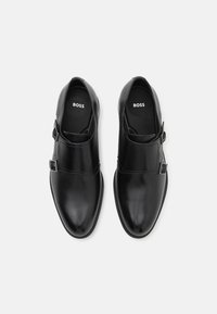 Black leather shoes with a smooth texture, rounded toes, and a buckle accent. "BOSS" logo on insoles; slip-on design without laces.