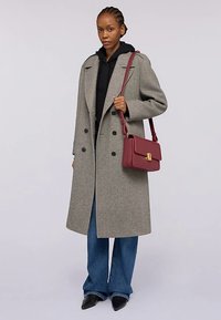 Grå ullrock med stora slag och dubbelradiga knappar, bärs över en svart hoodie. Kompletteras med en vinröd handväska och blå jeans.