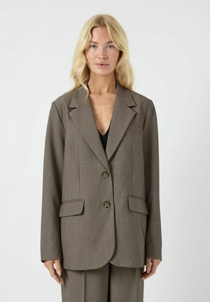 Brun skræddersyet blazer med en struktureret revers, to forlommer, to knapper og en glat tekstur. Bæres over en sort top.