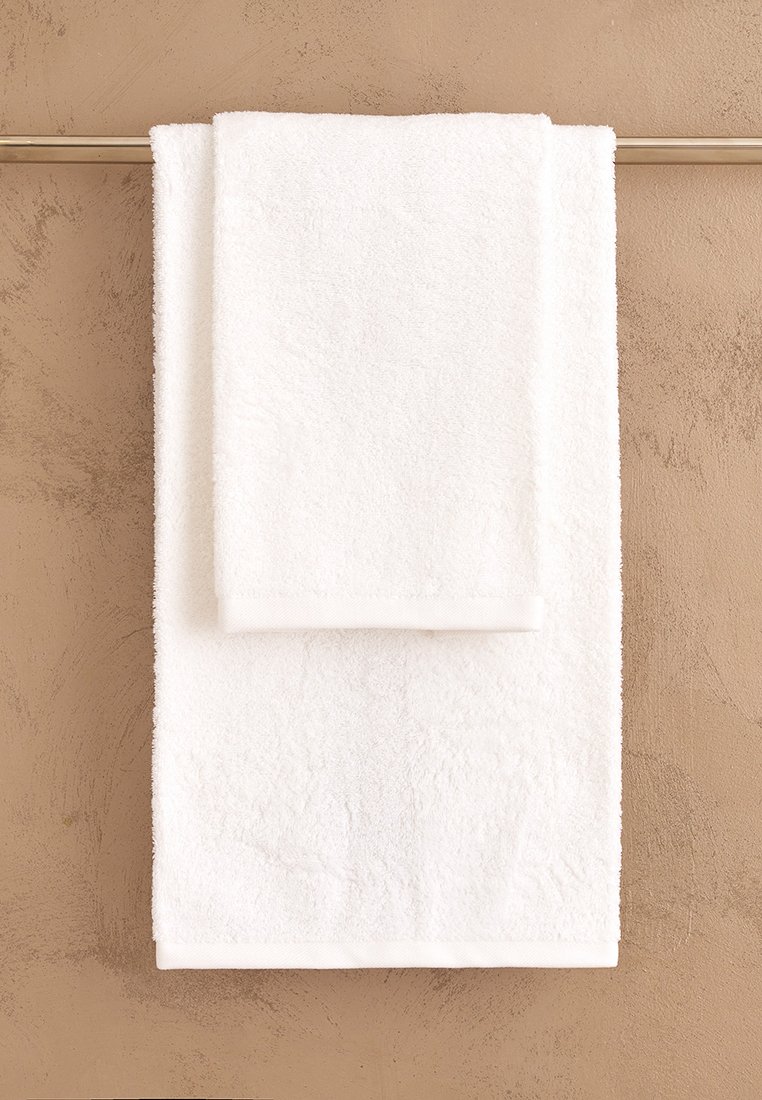 Asciugamano da bagno e asciugamano da mano in cotone bianco esposti su una barra, con una superficie morbida e testurizzata e bordi puliti su uno sfondo neutro.