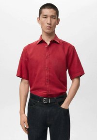 Rotes kurzärmliges Hemd mit Knopfleiste und klassischem Kragen, kombiniert mit schwarzer Denim-Jeans und einem schwarzen Gürtel, mit glatter Textur.