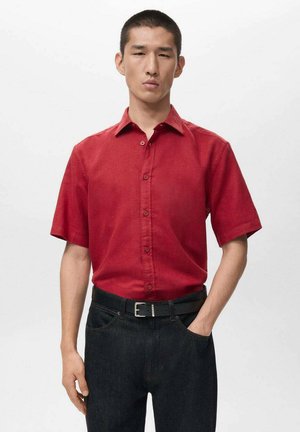 Rotes kurzärmliges Hemd mit Knopfleiste und klassischem Kragen, kombiniert mit schwarzer Denim-Jeans und einem schwarzen Gürtel, mit glatter Textur.