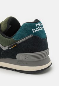 Černé a zelené semišové tenisky s šedými akcenty, obsahující logo "new balance" a branding ENCAP, zaoblený podpatek a texturovanou podrážku.