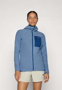 Lys blå zip-up fleecejakke med et teksturert mønster, hette og marineblå brystlomme. Har kontrastglidelåser og lange ermer.