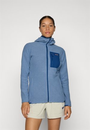 Lys blå zip-up fleecejakke med et teksturert mønster, hette og marineblå brystlomme. Har kontrastglidelåser og lange ermer.